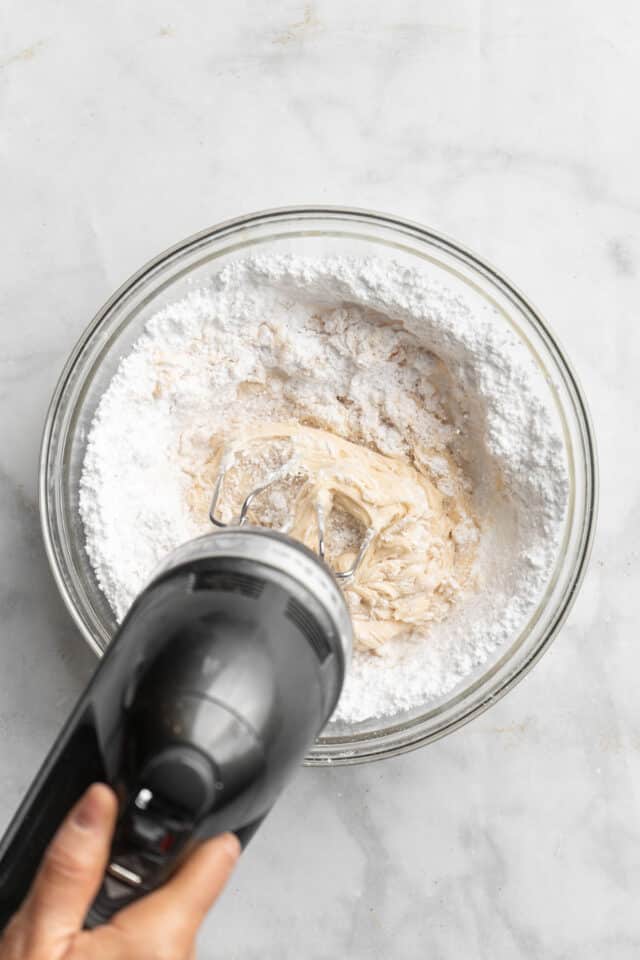 Mixing powdered sugar with butter and cream cheese mixture.