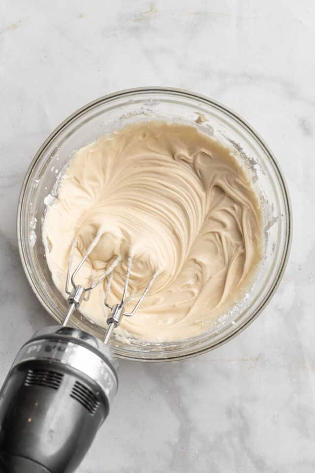 Using a handheld mixer to make cream cheese frosting.