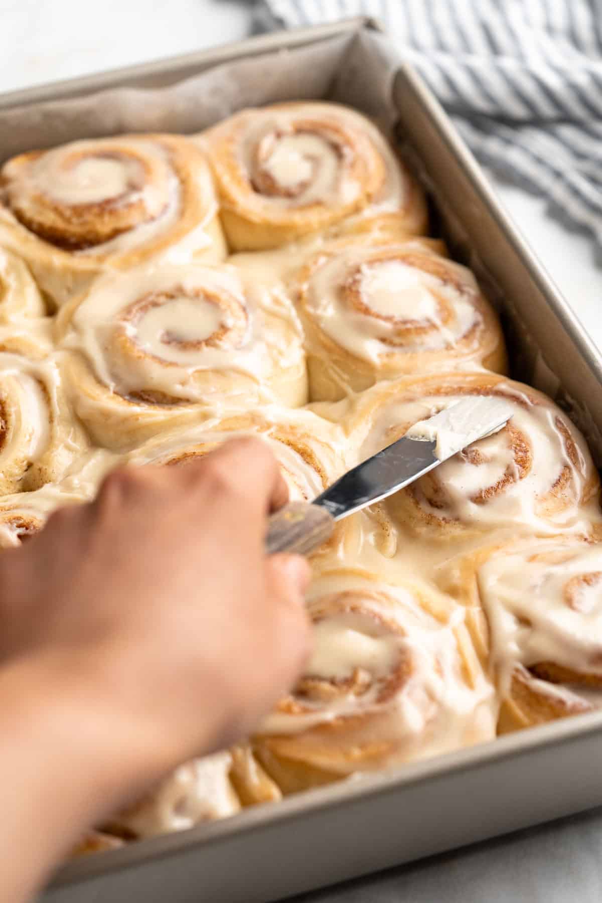 Using a knife to spread frosting on cinnamon rolls.