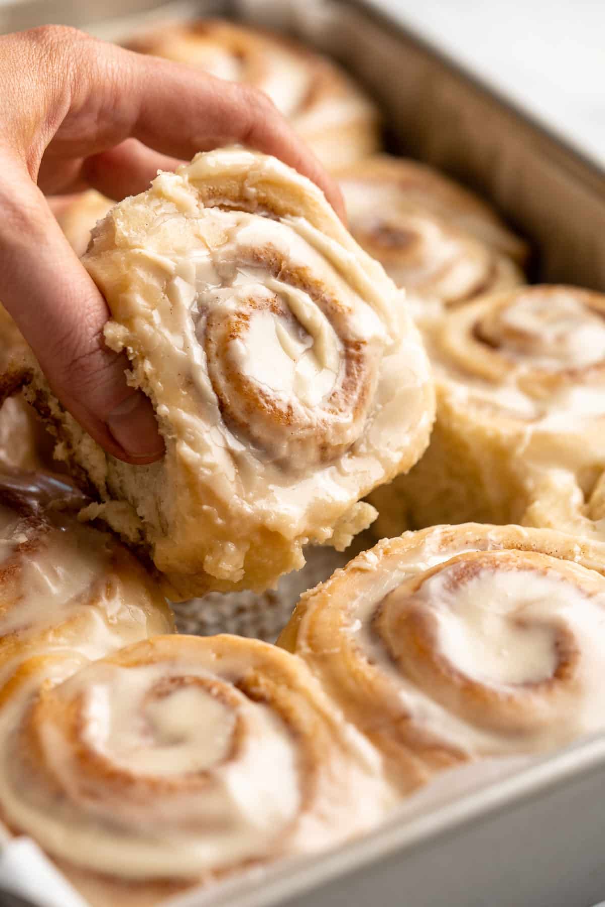 Pulling an iced cinnamon roll out of a baking pan.
