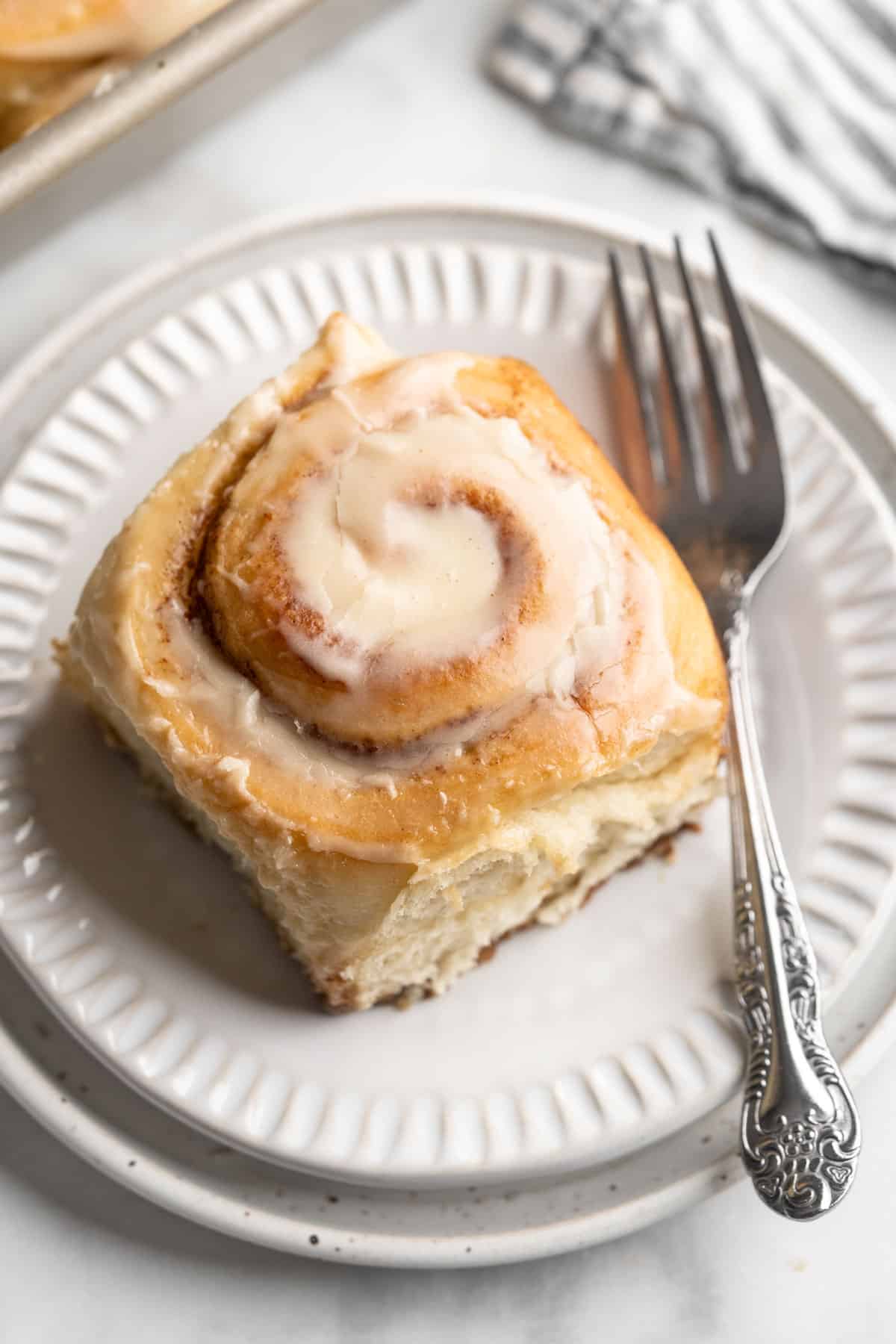 Cinnamon roll on a white plate with a fork.