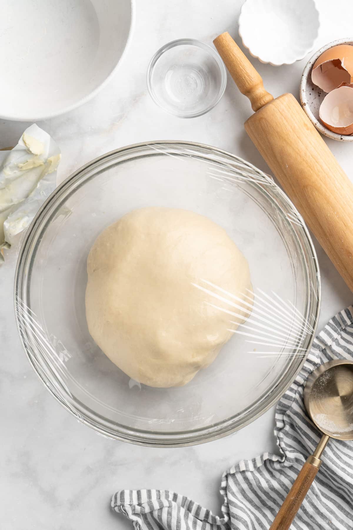 Covering dough ball in a bowl with plastic wrap.
