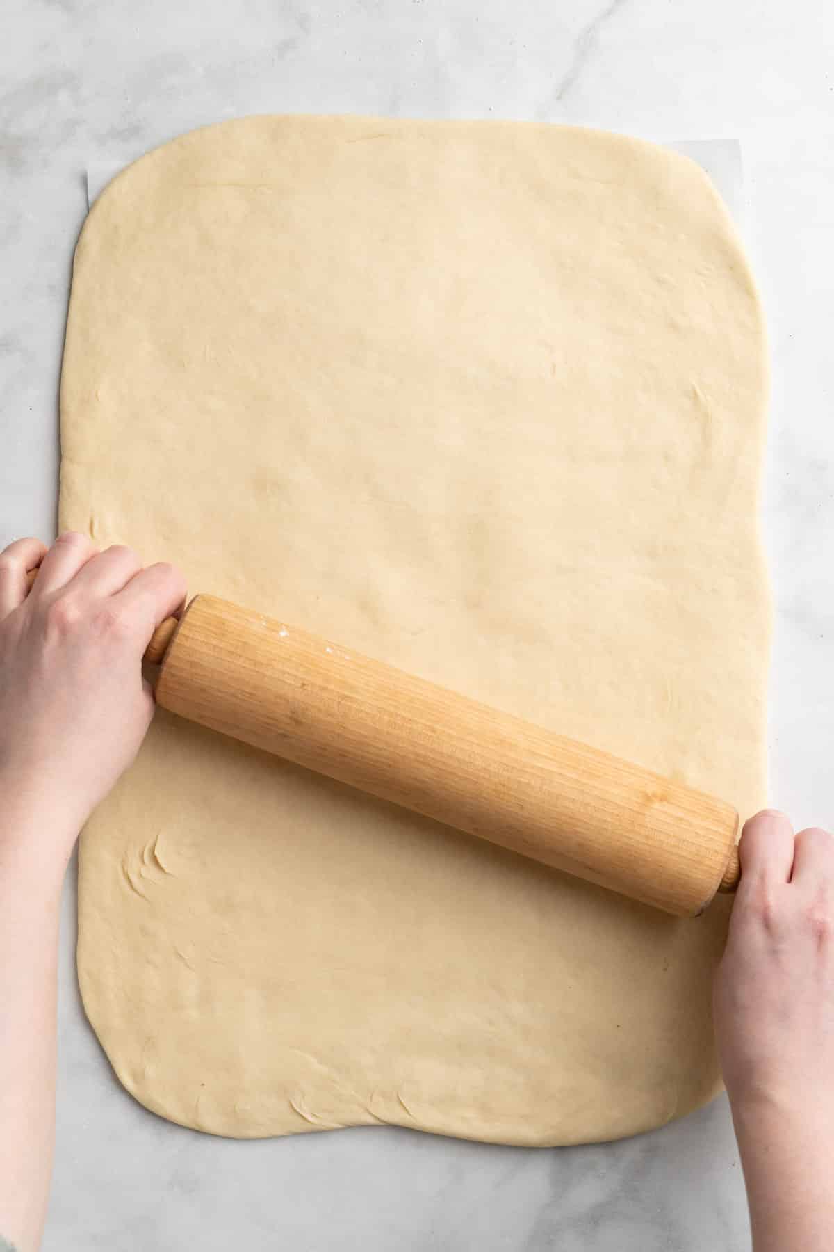Using a rolling pin to roll dough into a rectangle shape.