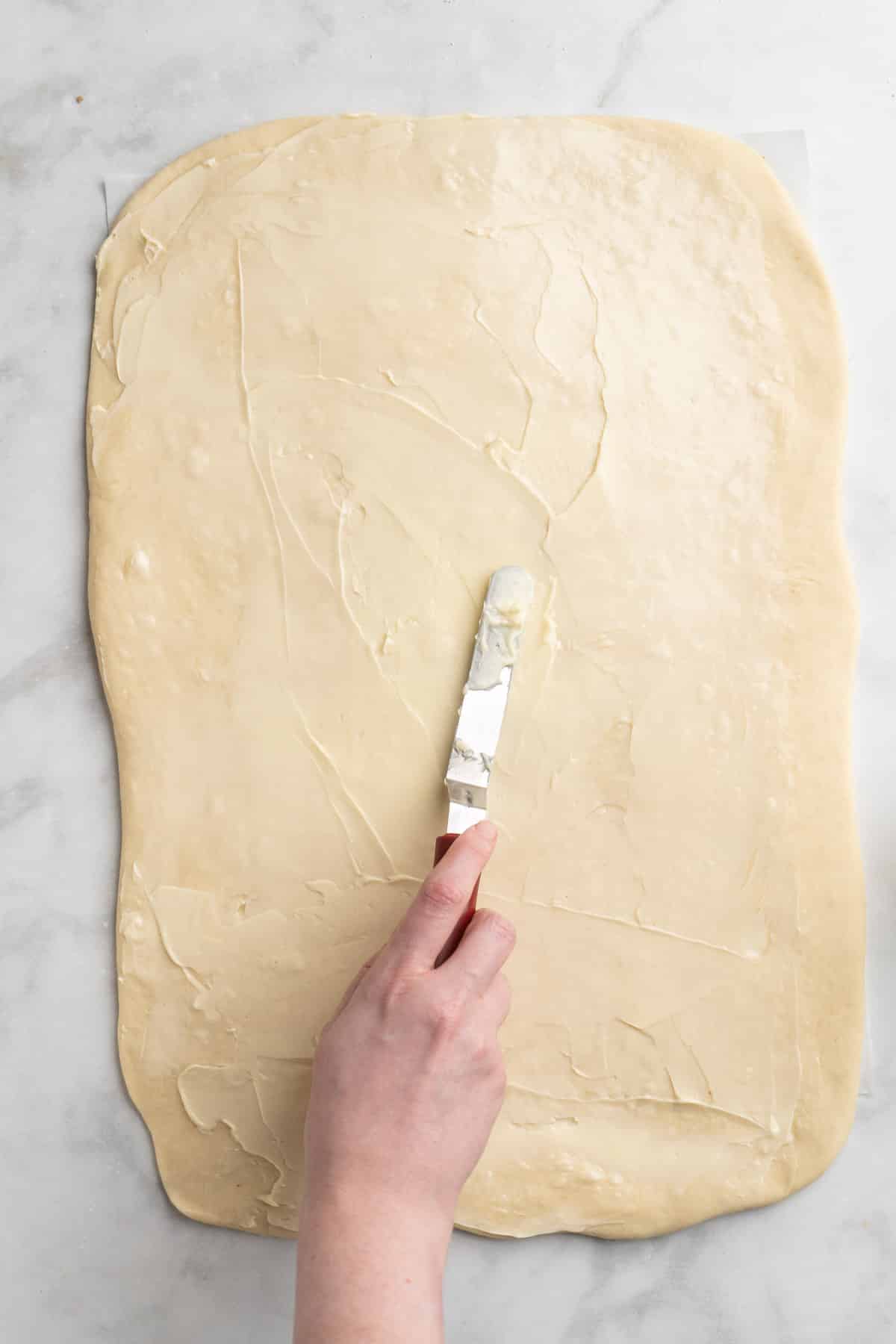 Spreading butter over dough.