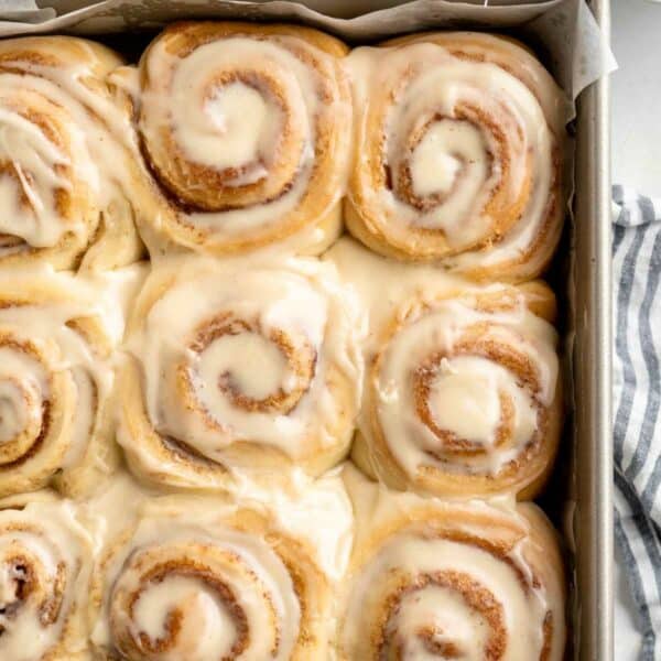 Iced cinnamon rolls in a parchment-lined pan.