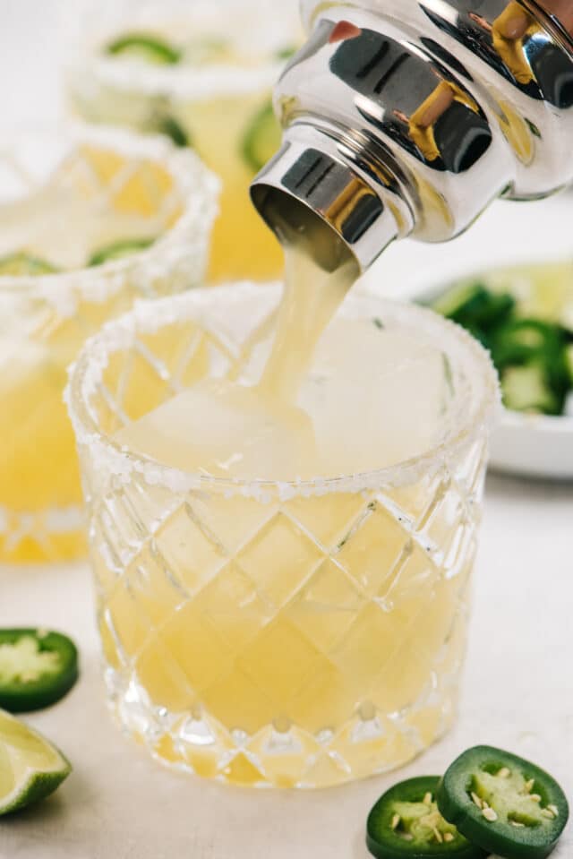 Pouring a margarita from a cocktail shaker into a glass.