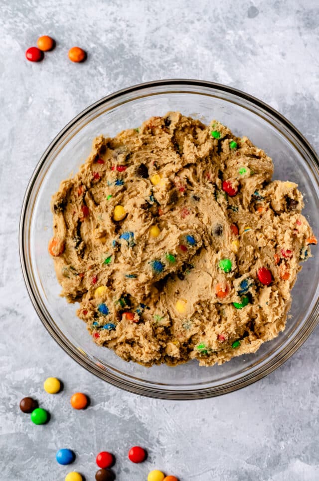 cookie dough mixed in a large glass mixing bowl for M&M cookies
