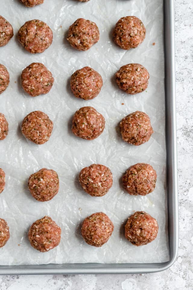 Rolled meatballs on a large baking sheet lined with parchment paper.