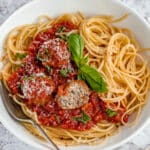 turkey meatballs over pasta in a white bowl