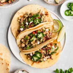 Vegan tacos on a white plate served with lime wedges.