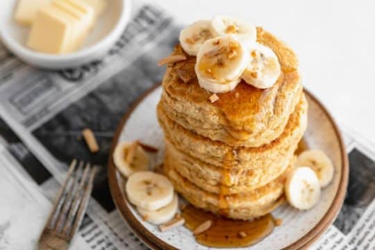 stack of whole wheat pancakes topped with banana slices and syrup