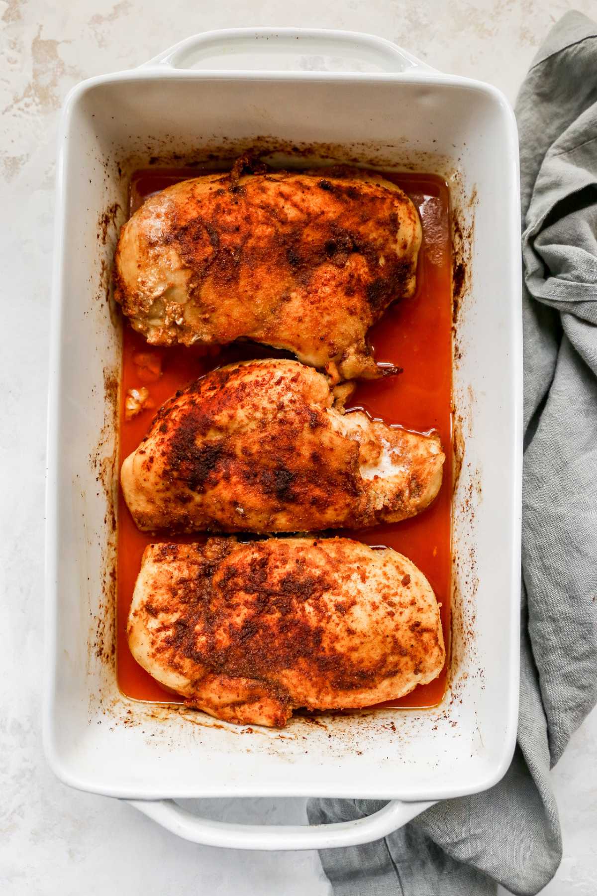 Three chicken breasts baked in a white casserole dish.