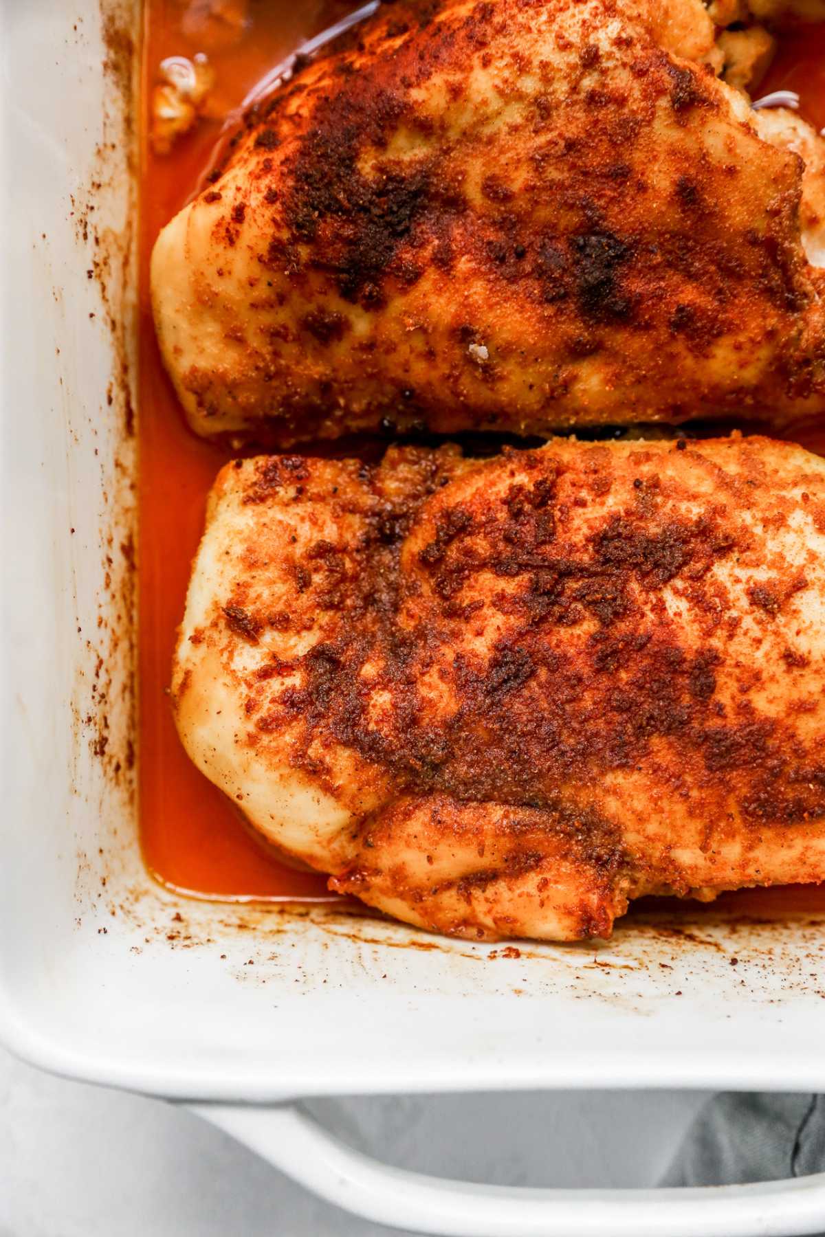 Closeup view of two seasoned chicken breasts in a dish.
