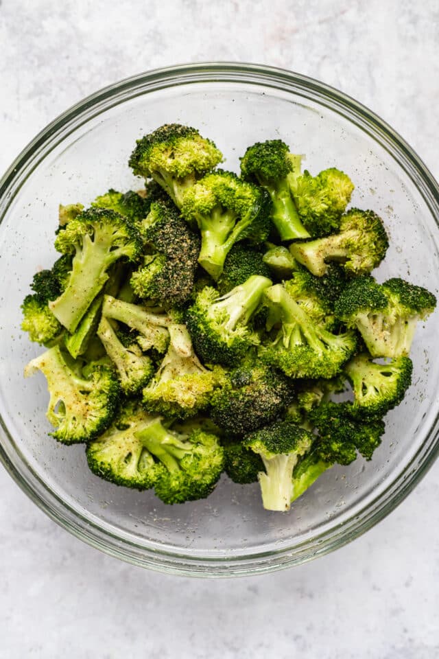 broccoli florets in a large glass mixing bowl, tossed with seasoning