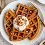 pumpkin waffles on a white plate served with yogurt, chopped pecans and syrup