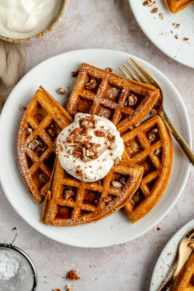 pumpkin waffles on a white plate served with yogurt, chopped pecans and syrup