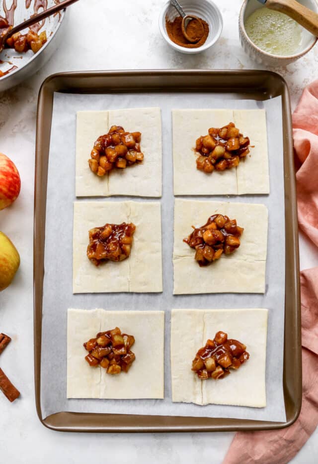 Adding apple filling over puff pastry squares.