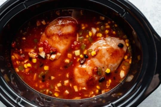 chicken breasts cooking with corn, beans and tomatoes in a crockpot