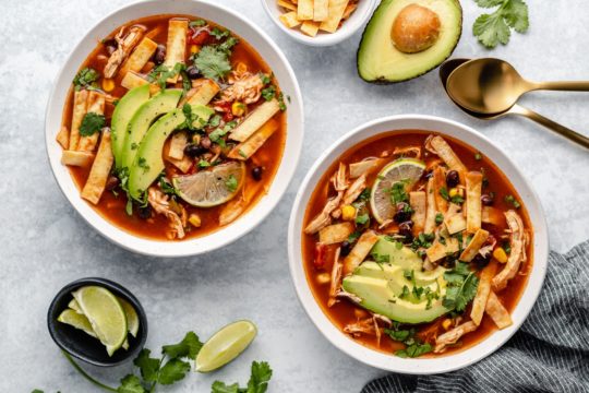 crockpot chicken tortilla soup in two bowls garnished with avocado and tortillas