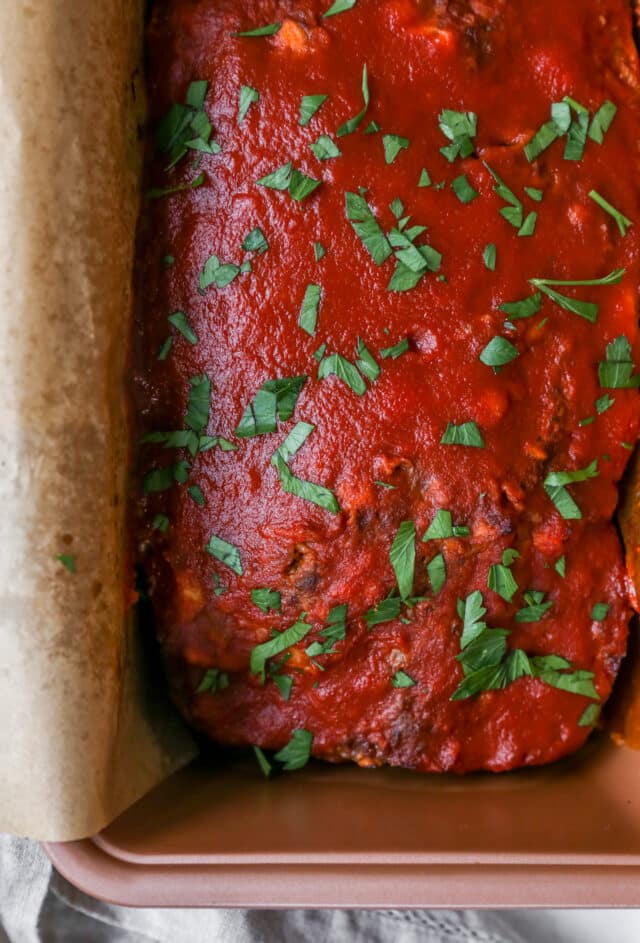 cooked meatloaf in loaf pan topped with fresh parsley