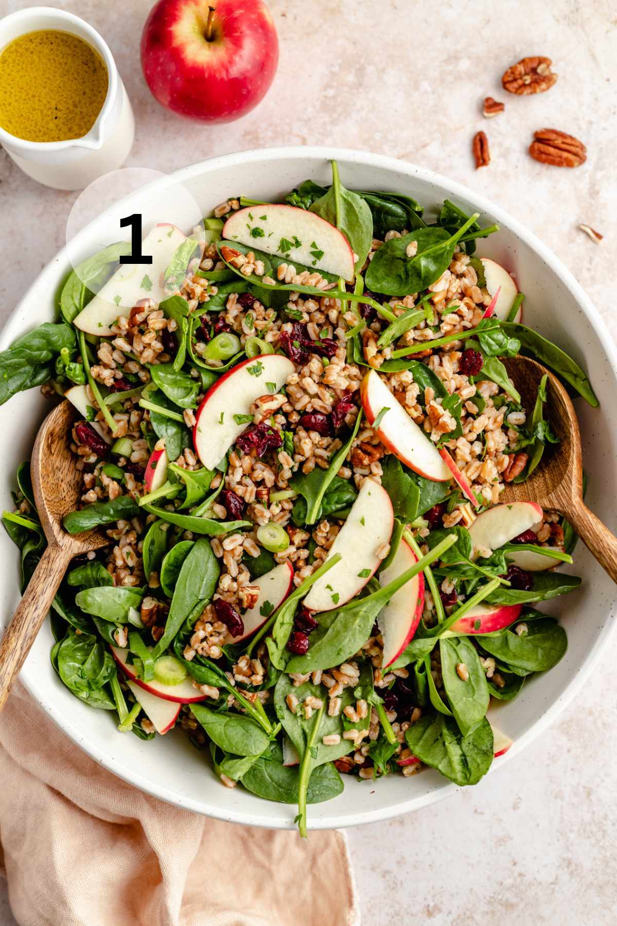 Using large wooden spoons to toss a salad with spinach, farro and apple slices.