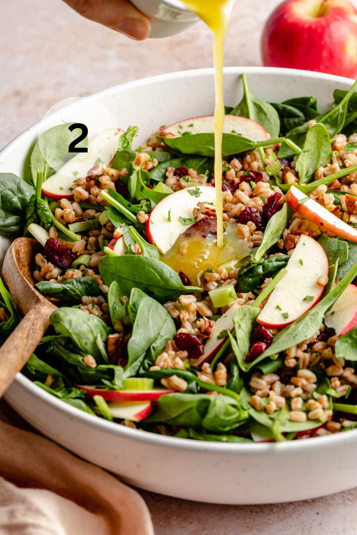 Drizzling dressing over apple farro salad.