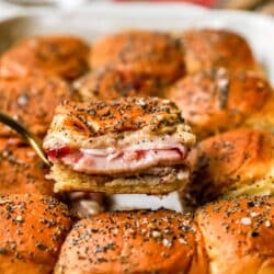 Serving turkey sliders from a baking dish with turkey, cheese and cranberry sauce.