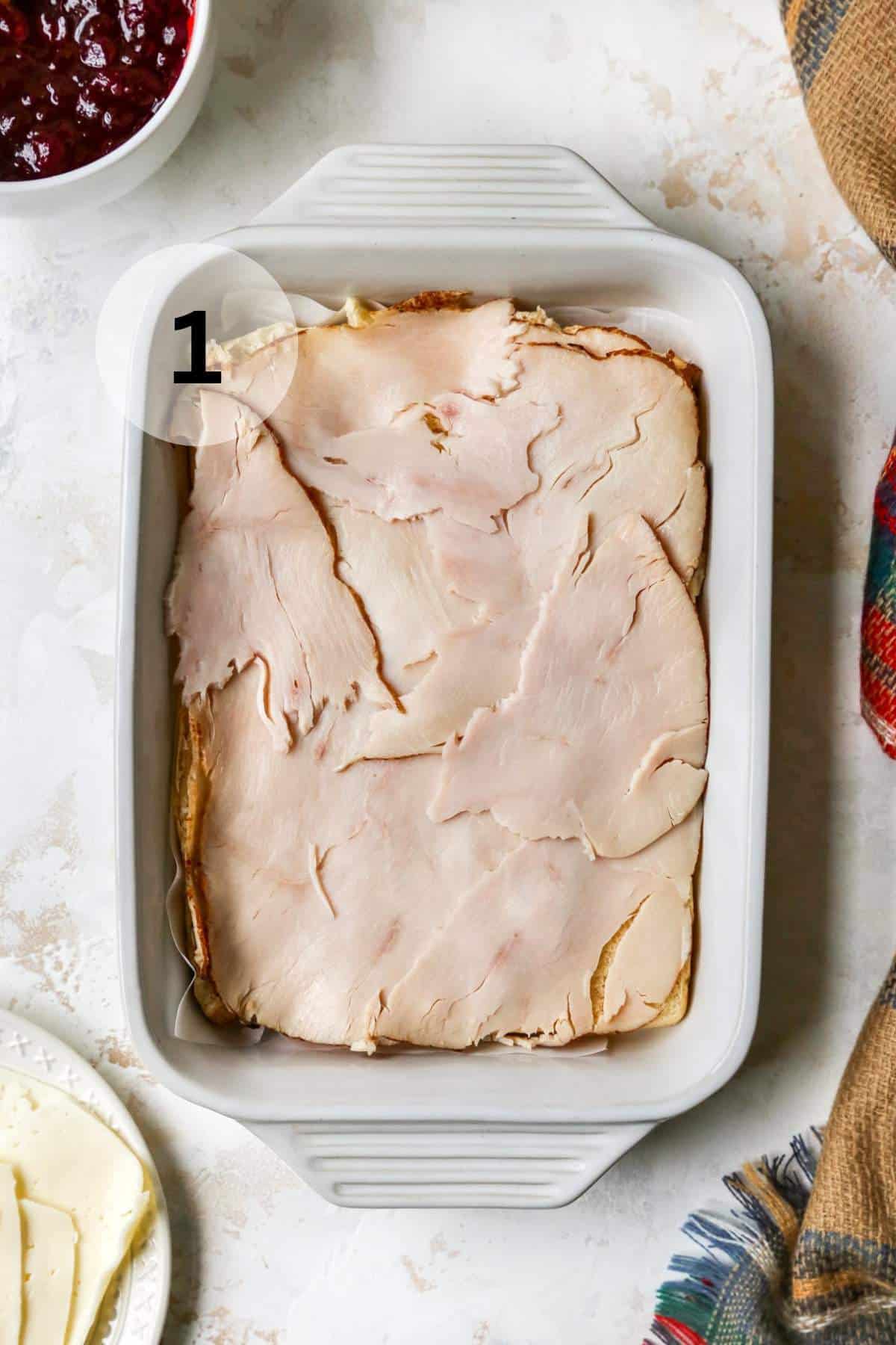 Sliced turkey over Hawaiian rolls in a white baking dish.