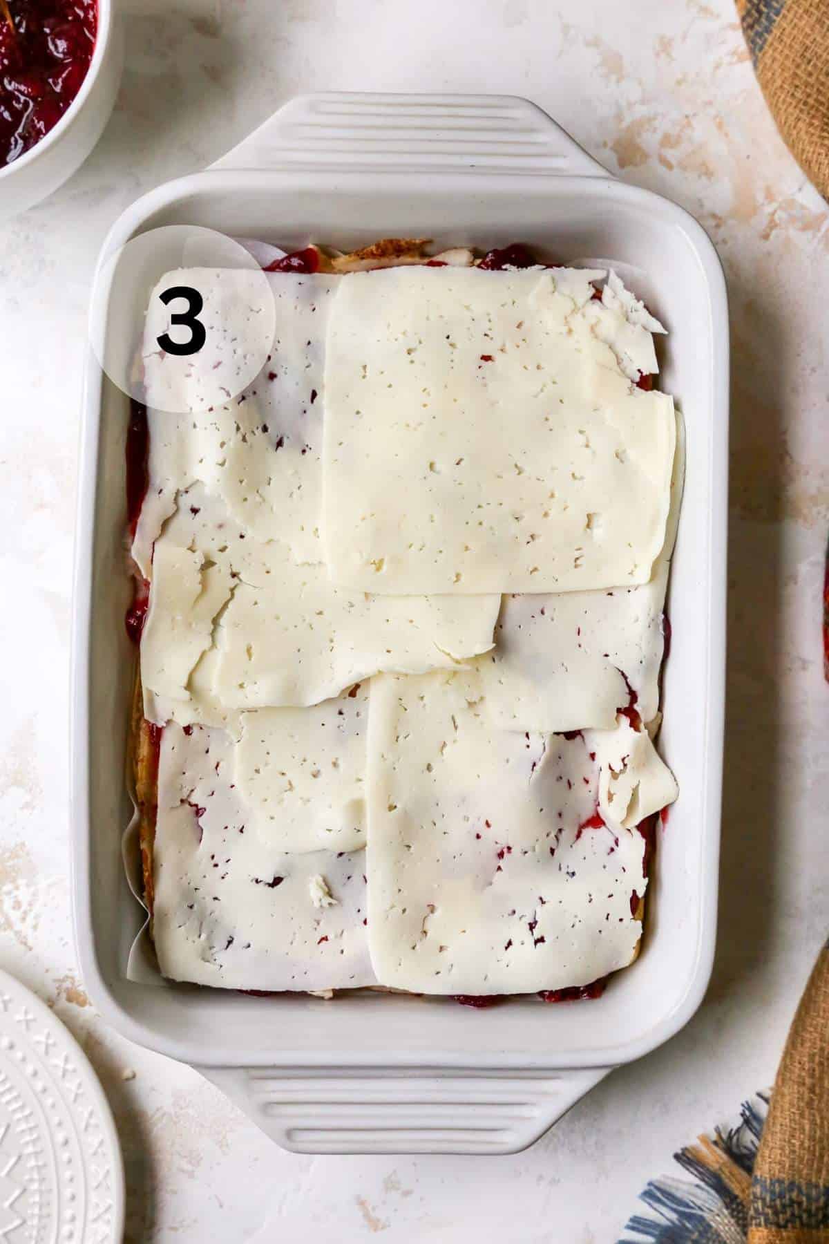 Slices of Swiss cheese layered over turkey slices and cranberry sauce in a white dish.