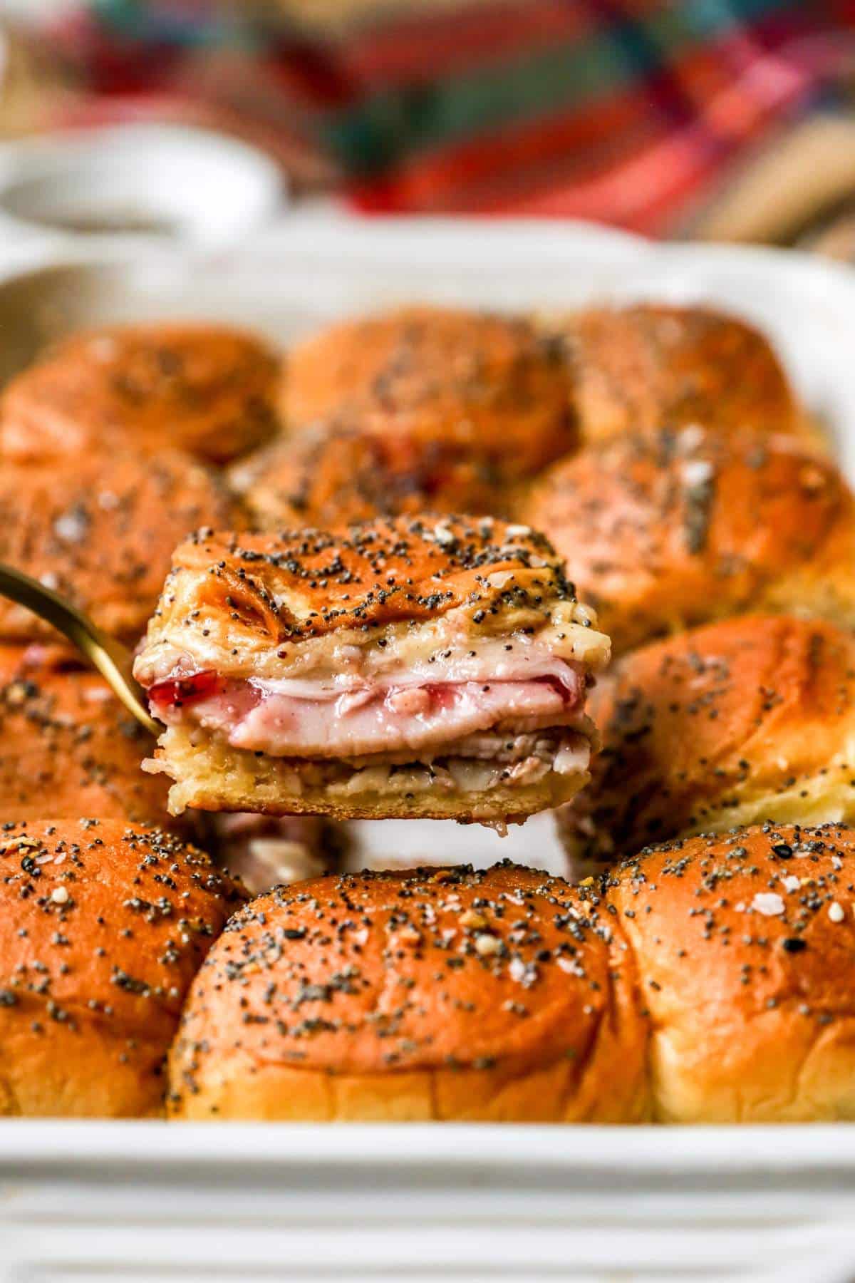 Serving turkey sliders from a baking dish with turkey, cheese and cranberry sauce.