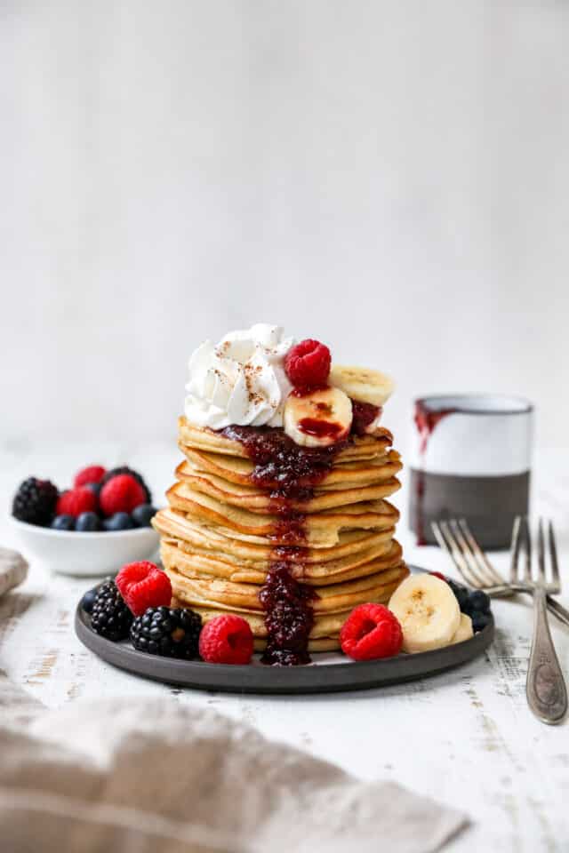 pancakes stacked high on a plate with fruit 