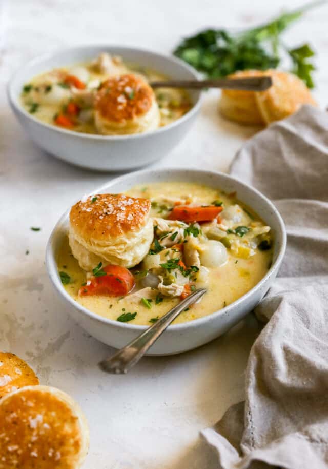 chicken pot pie soup in a white bowl topped with a biscuit
