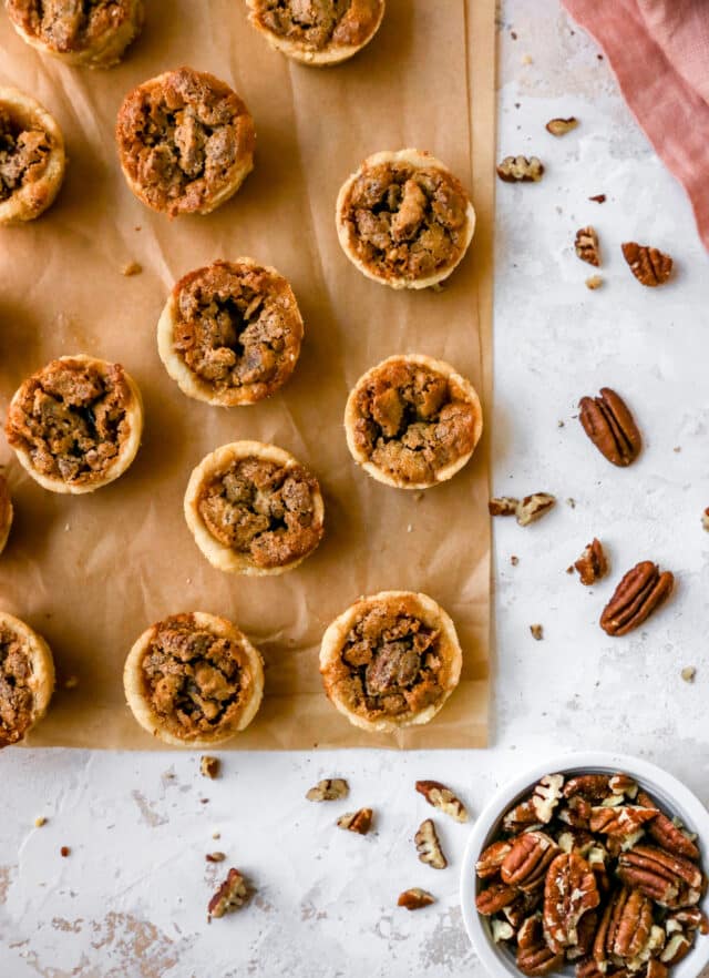 mini pecan pies on parchment paper near a bowl of chopped pecans