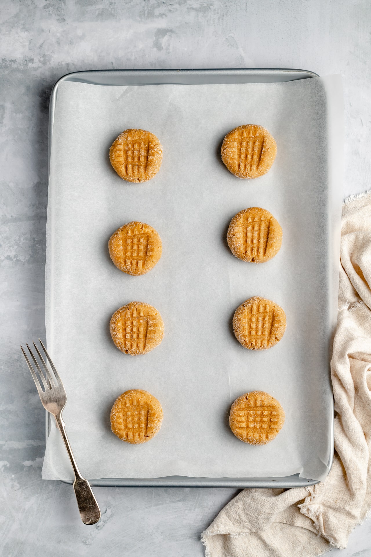 peanut butter cookie dough on a baking sheet with fork imprints on the tops
