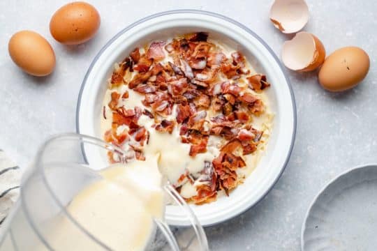 pouring milk and egg mixture over cooked crumbled bacon