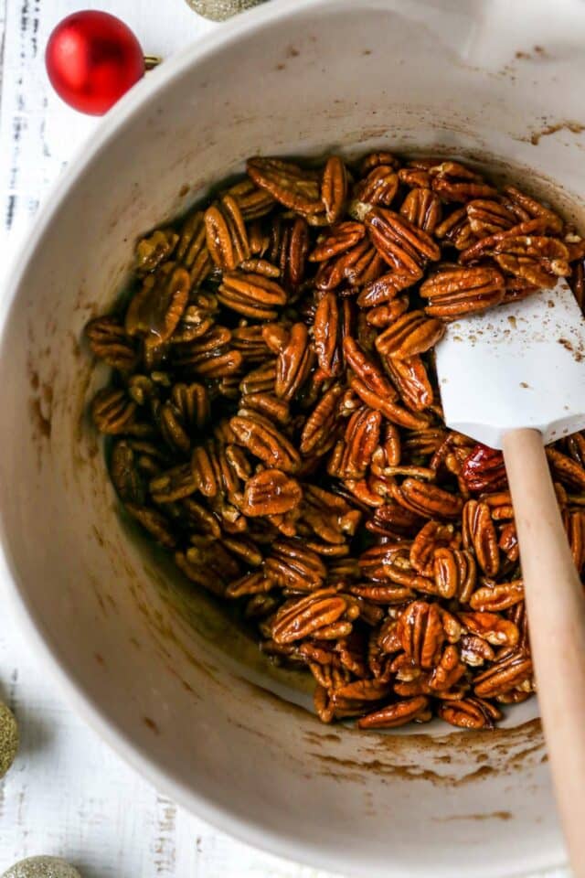 Stirring pecans with butter and spices in a large bowl.