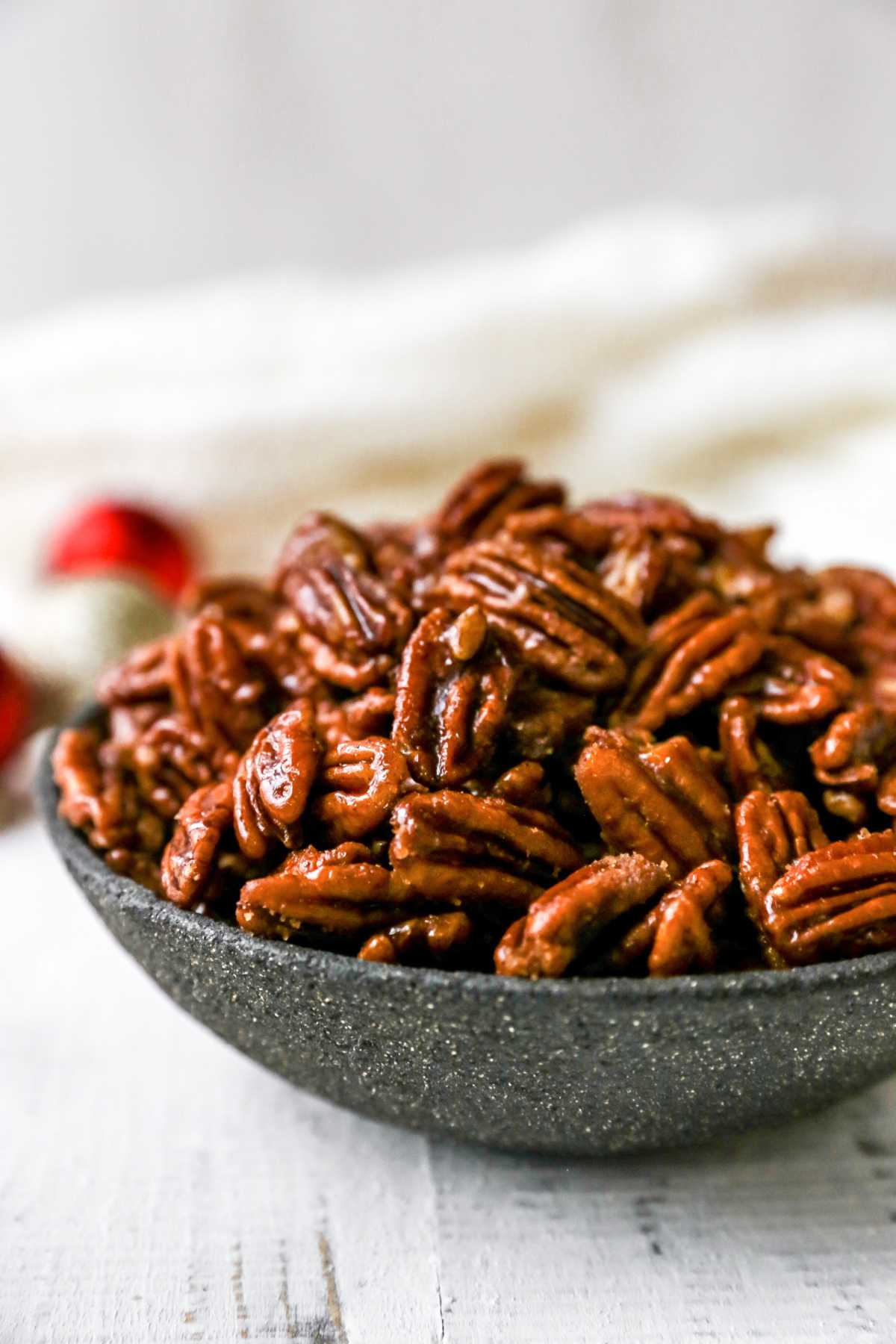 Side view of glazed pecans in a dark-colored bowl.