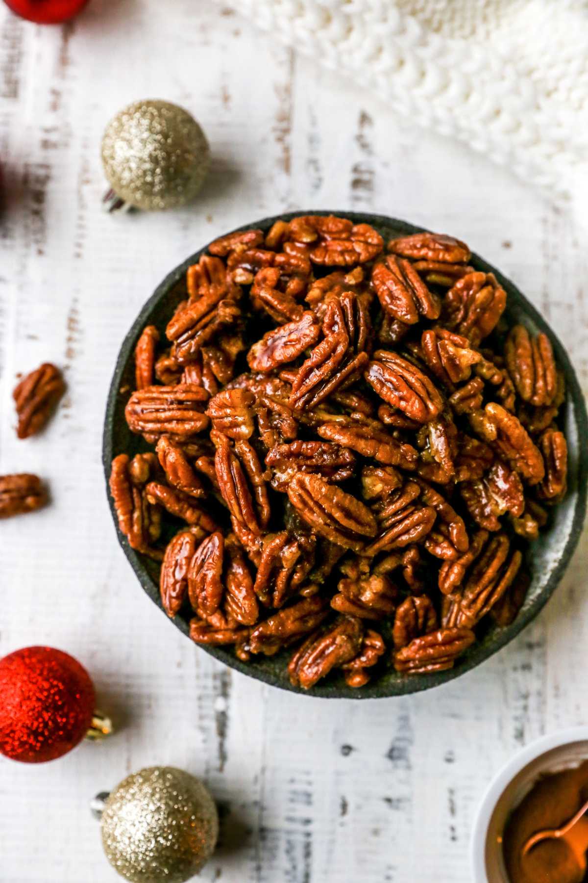 Candied pecans in a bowl near Christmas ornaments. 