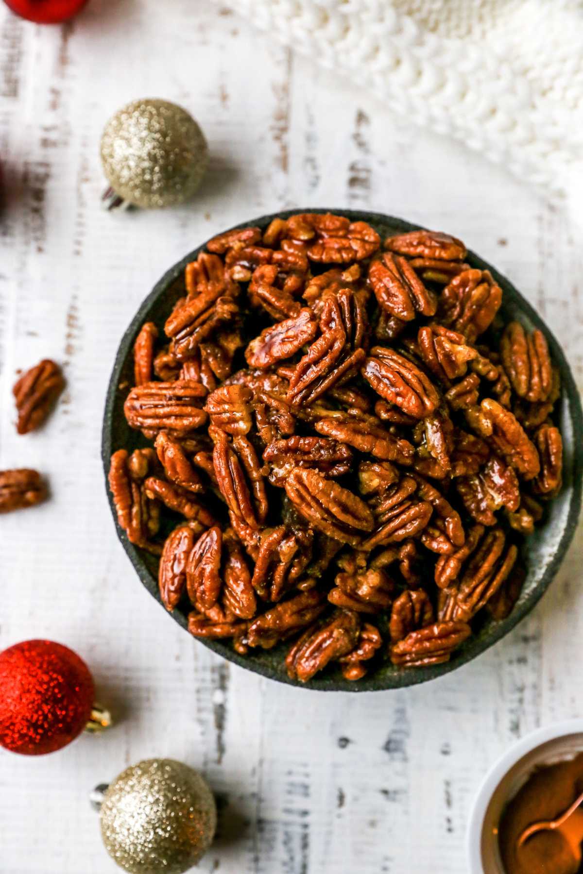 Candied pecans in a bowl near Christmas ornaments.