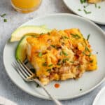 serving of breakfast casserole served on a small white plate with a fork and sliced avocado