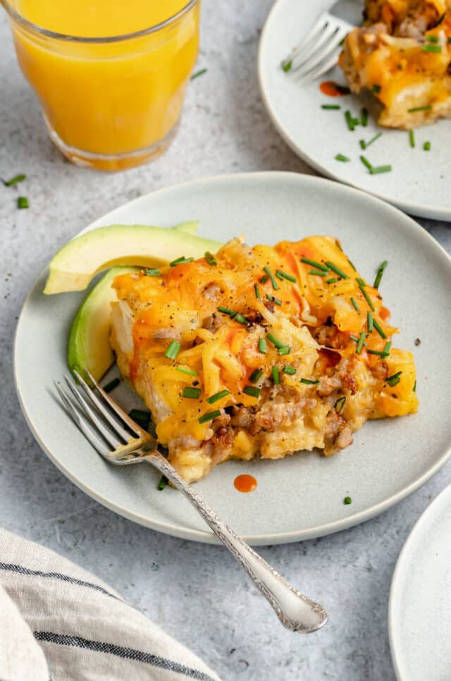 serving of breakfast casserole served on a small white plate with a fork and sliced avocado