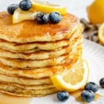 Stack of lemon ricotta pancakes topped with blueberries, syrup and sliced lemon.