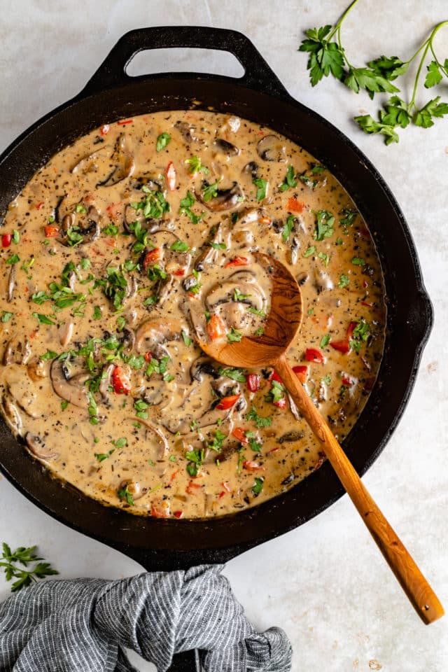 Mushroom cream sauce in a large skillet with a wooden spoon.