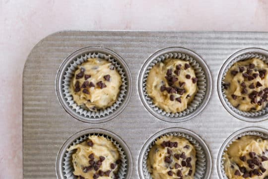 filling muffin tins with muffin batter and adding chocolate chips to the tops