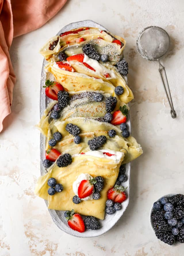 folded crepes with whipped cream and berries on a serving plate