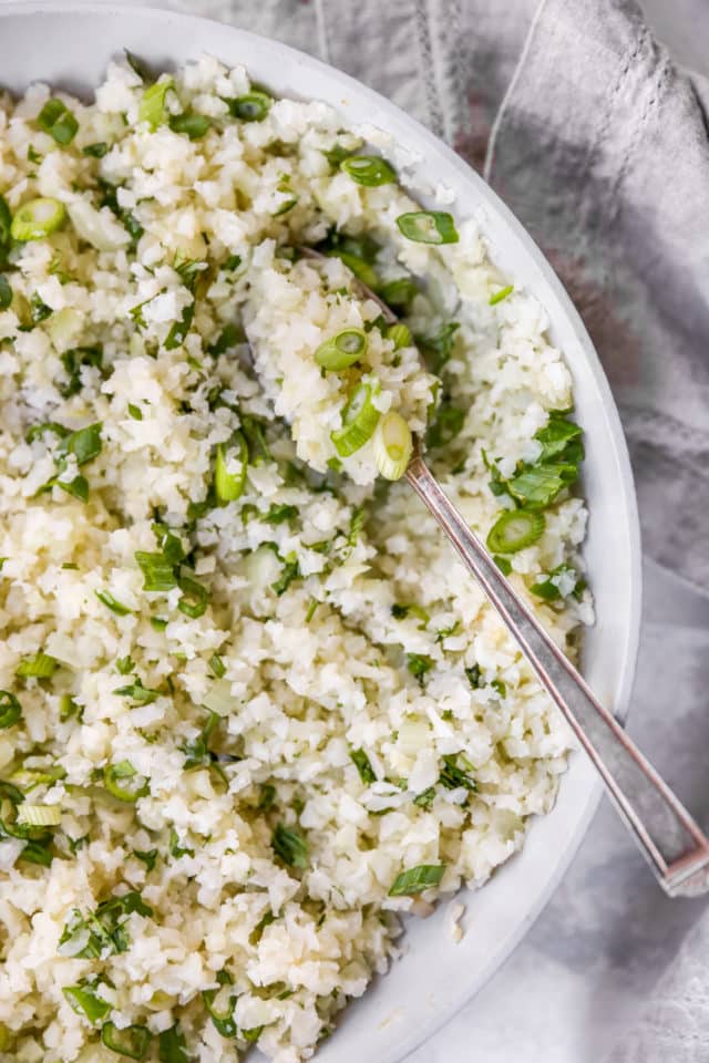 serving cauliflower rice out of a skillet with a spoon
