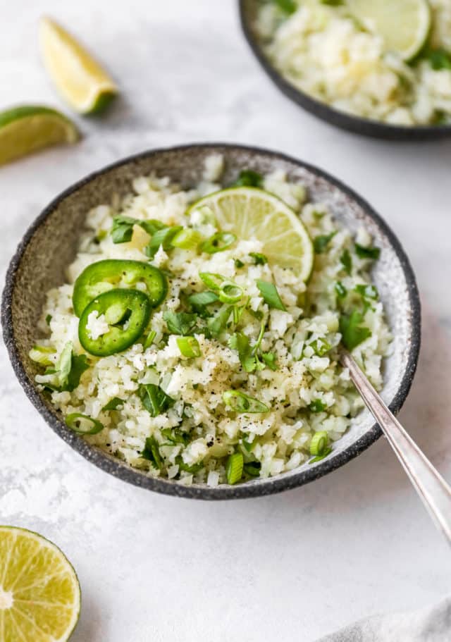 small bowl with cilantro lime cauliflower rice topped with a lime wedge and sliced jalapeño 