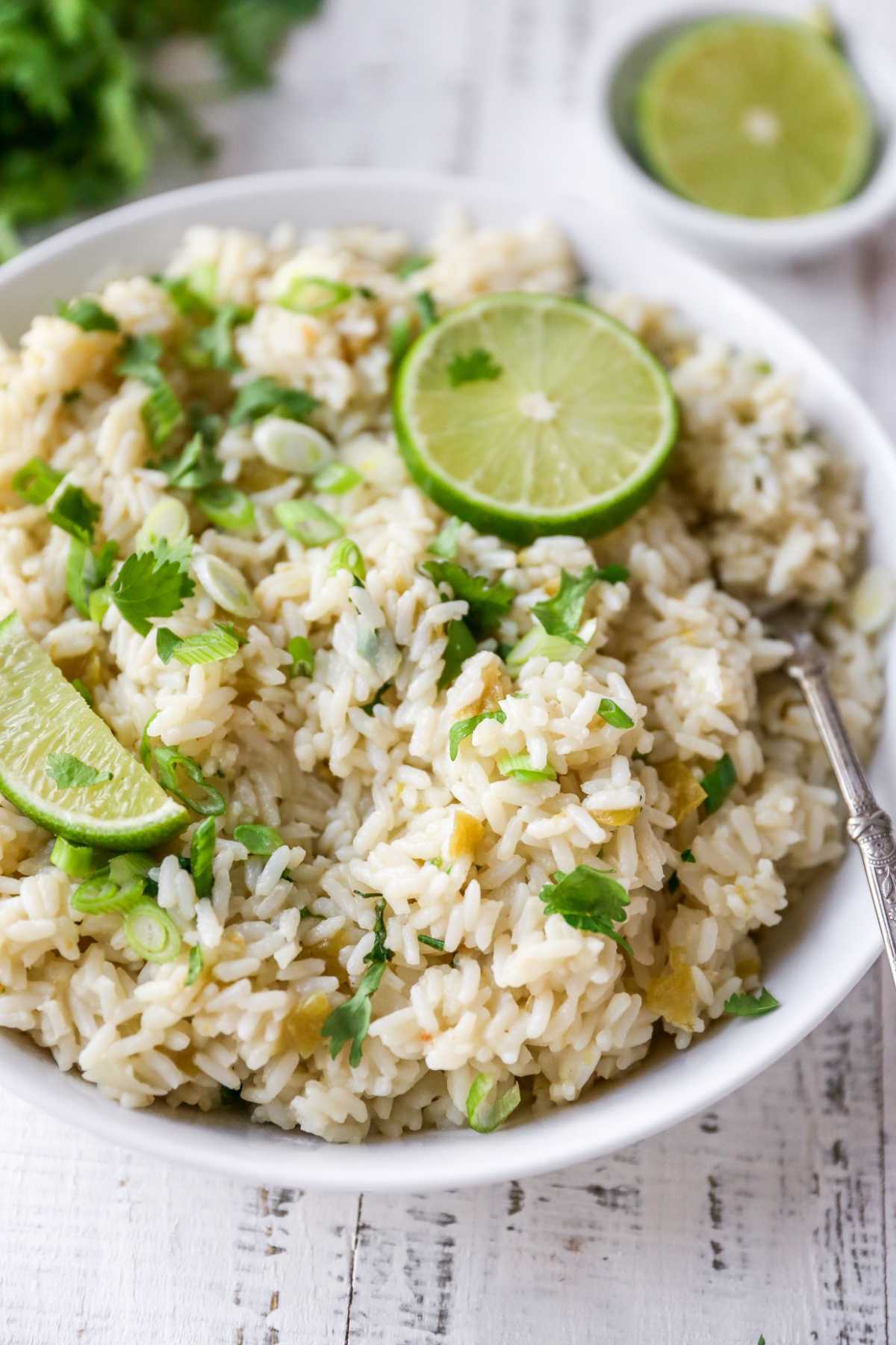 Cilantro lime rice in a white bowl near lime wedges and a bunch of fresh cilantro.