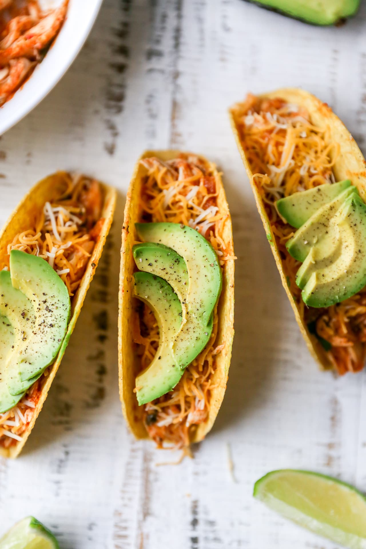 Crockpot salsa chicken served in taco shells with cheese and sliced avocado.
