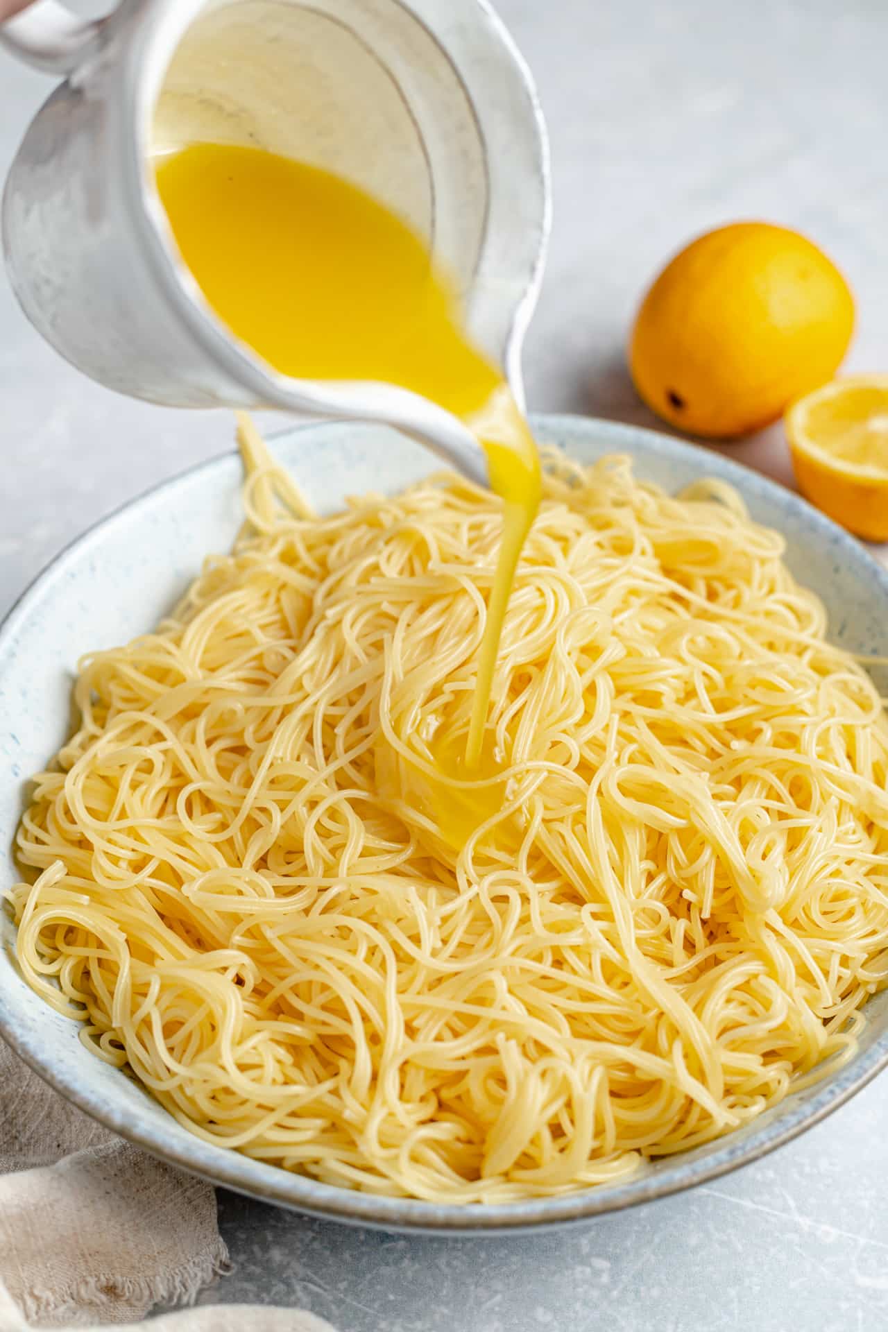 Pouring lemon dressing over bowl of noodles.